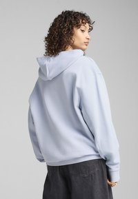 Felpa azzurra con cappuccio, maniche lunghe, vestibilità comoda e texture morbida. Abbinata a pantaloni grigio scuro, con un focus sullo stile casual.