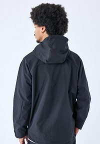 Giacca nera impermeabile, con cappuccio, maniche lunghe e tessuto testurizzato. Il design presenta cuciture minime e una silhouette moderna e funzionale.
