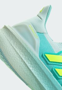 Baskets de sport bleu clair avec une tige texturée, une épaisse semelle intermédiaire blanche et de vives accents jaunes sur le côté et le talon.