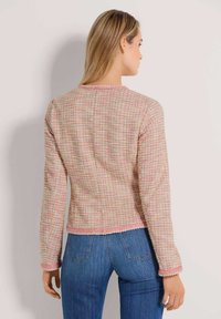 Rosa- und cremefarben karierte Jacke mit langen Ärmeln, strukturiertem Stoff und kontrastierendem Besatz entlang des Ausschnitts und Saums. Figurbetonte Passform.