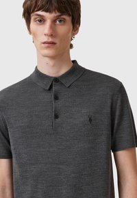 Grau-poloshirt aus weichem Strickstoff, mit Kragen, einer Drei-Knopf-Leiste, kurzen Ärmeln und einem kleinen dunklen Logo auf der Brust.