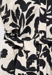 Robe en tissu à motif floral noir et blanc avec des boutons, une taille ceinturée et un matériau texturé. Présente des motifs de feuilles abstraites.