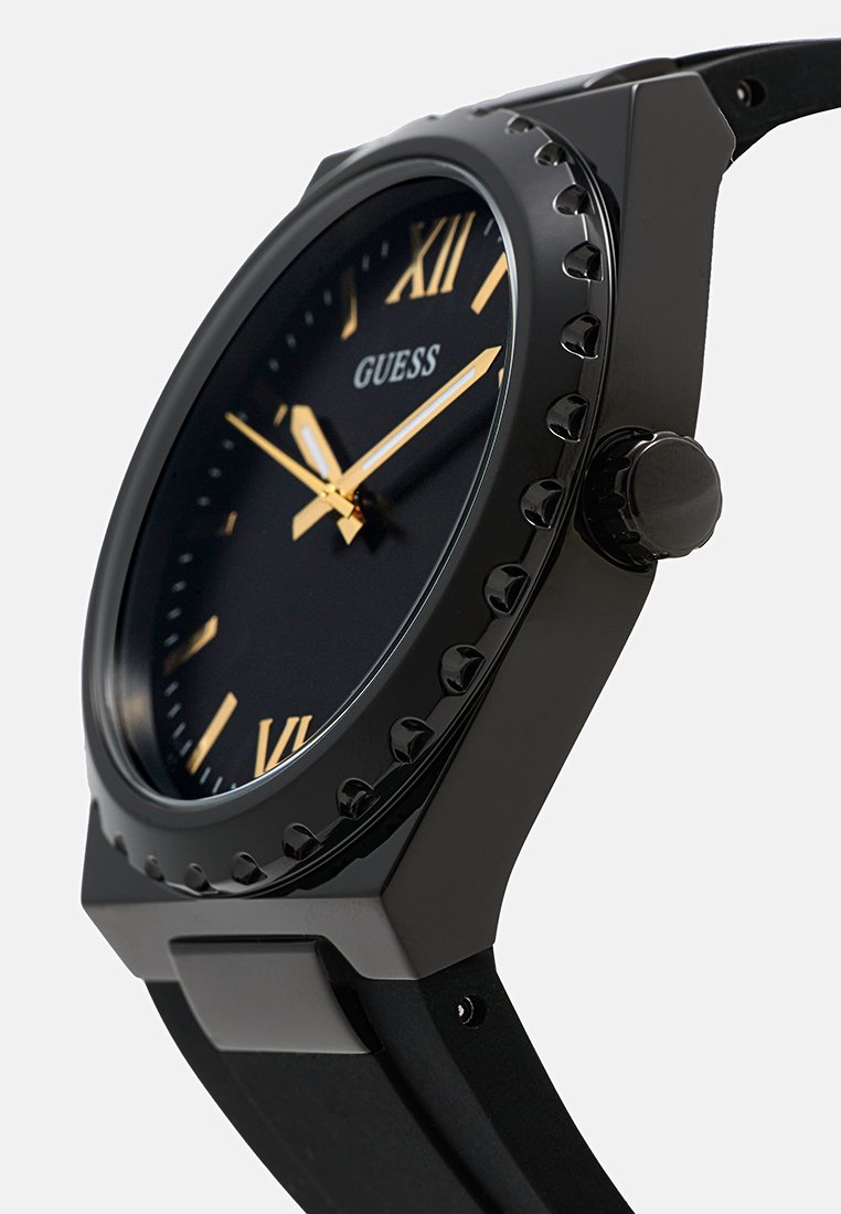 Reloj analógico negro con números romanos dorados y manecillas, correa de goma y bisel texturizado. Logo de la marca mostrado en la esfera.