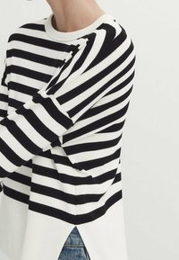 Mustavalkoinen vaakaraitainen pitkähihaiset paita, jossa on olkatoppaukset ja sivuhalkio, päälläsiniset farkut.