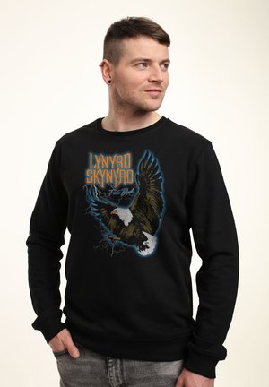 Czarna bluza z grafiką orła w niebieskich detalach oraz napisem "Lynyrd Skynyrd" w pomarańczowym kolorze. Długie rękawy z ściągaczami.