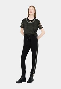 Črne hlače s stransko črto, kombinirane s črnim bleščečim topom z čipkastimi rokavi in okroglim izrezom z belo obrobo.