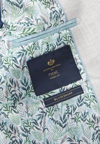 Doublure de veste à motif floral avec deux étiquettes en tissu, l'une marine avec le texte doré "next skinny fit", l'autre plus petite avec "#LOOKSHARP" en doré.