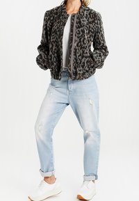 Giacca bomber con stampa leopardata in morbido tessuto, motivo grigio e nero, con zip frontale, abbinata a jeans chiari strappati e sneakers bianche.