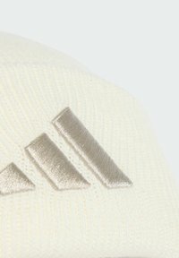 Krémový pletený čiapka s ryhovanou textúrou a kovovosivým logom s tromi diagonálnymi pruhmi vyšitými na prednej strane.