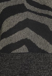 Pull en maille présentant un motif à rayures zèbre en noir et argent métallisé, avec une texture douce et un ourlet côtelé noir uni.