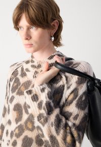 Pull en tricot à motif léopard dans des tons crème, marron et gris. Doté d'un col et de poignets côtelés, avec une texture douce. Sac à main noir porté sur l'épaule.