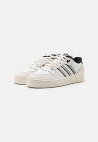White leather sneakers with black accents, three black stripes on the side, round toe, lace-up design, and textured rubber sole.