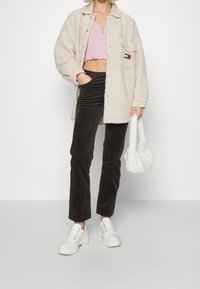 Veste en polaire crème, crop top rose clair, pantalon en velours côtelé sombre, baskets blanches épaisses et un sac à main fluffy blanc.