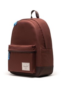 Smeđa tkanina ranac s zakrivljenim oblikom, plavim patentnim zatvaračima, prednjim džepom i logotipom. Tekstura površine s podesivim trakama.