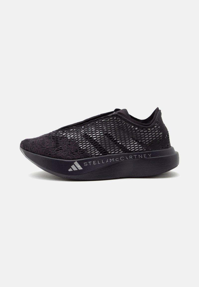 Μαύρο αθλητικό παπούτσι slip-on με πλέγμα επάνω, λεπτομέρειες από λουλουδένια δαντέλα, παχιά σόλα με λογότυπα Adidas και Stella McCartney, πλευρική όψη.