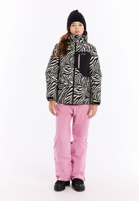 Zebrahunkoisen puhaltimen takki mustassa ja kermaisessa väriyhdistelmässä, jossa on musta rintatasku ja vaaleanpunainen vetoketju; yhdistettynä vaaleanpunaisiin hiihtohousuihin ja mustiin saappaisiin.