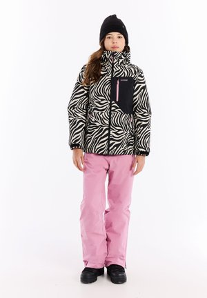 Zebra-musterte Pufferjacke in Schwarz und Creme mit einer schwarzen Brusttasche und pinkem Reißverschluss; kombiniert mit pinken Skihosen und schwarzen Stiefeln.