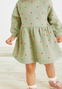 Abito verde a maniche lunghe con scollo rotondo, caratterizzato da piccole arcobaleni ricamati in rosa e arancione, e una gonna svasata.