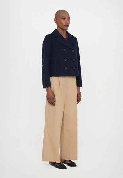 Giacca cropped doppiopetto in misto lana di colore navy, con ampi risvolti e due tasche frontali. Abbinata a pantaloni beige a gamba larga e ballerine nere.