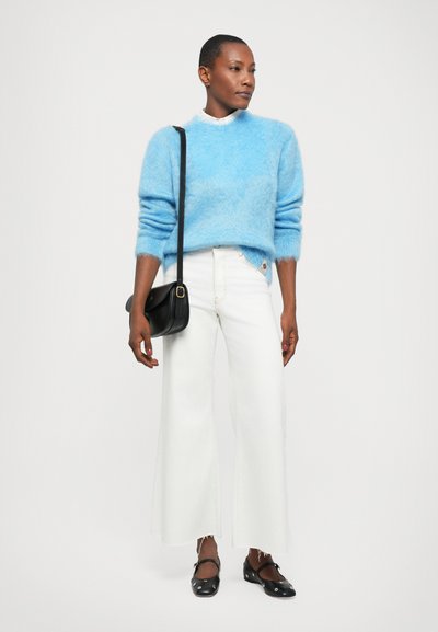 Pull en peluche bleu clair avec des manches longues, assorti à un jean blanc à jambes larges. Sac bandoulière noir et chaussures plates noires avec bout arrondi.