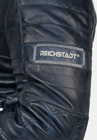 Marlijne leren jackmouw met een gequiltte textuur, zilveren stiksels en een prominente grijze label met het "REICHSTADT™" merk.