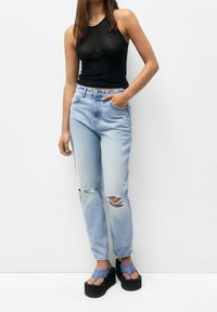 Svart ärmlös topp, ljusblå rivna jeans och svarta plattformssandaler med blå remmar. Avslappnad passform med fransade fållar och en avslappnad siluett.