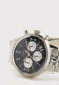 Relógio cronógrafo Timex Marlin prateado com mostrador preto, três submostradores, tacómetro, janela de data e bracelete de metal sobre fundo branco.