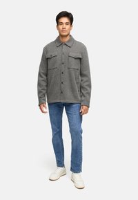 Grå stribet jakke med to brystlommer, knaplukning og tekstureret stof, parret med blå jeans og hvide sneakers.