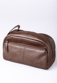 Brown leather toiletry bag with a smooth texture, featuring a zippered main compartment, front pocket, and a convenient carry handle.