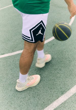 Pantaloni scurți de baschet alb-negru cu un design în formă de diamant și logo. Adidași de culoare deschisă cu un model spiralat și linii de accent. Mingea de baschet în mișcare.