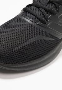 Czarne buty sportowe z siateczkową cholewką, gładkimi akcentami, teksturowaną powierzchnią i zaokrągloną podeszwą. Wyraźne sznurowadła dodają charakteru projektowi.