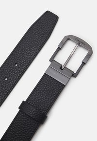 Cintura in pelle nera con finitura testurizzata, dotata di una fibbia rettangolare in argento opaco. Include fori di regolazione e un anello in pelle.