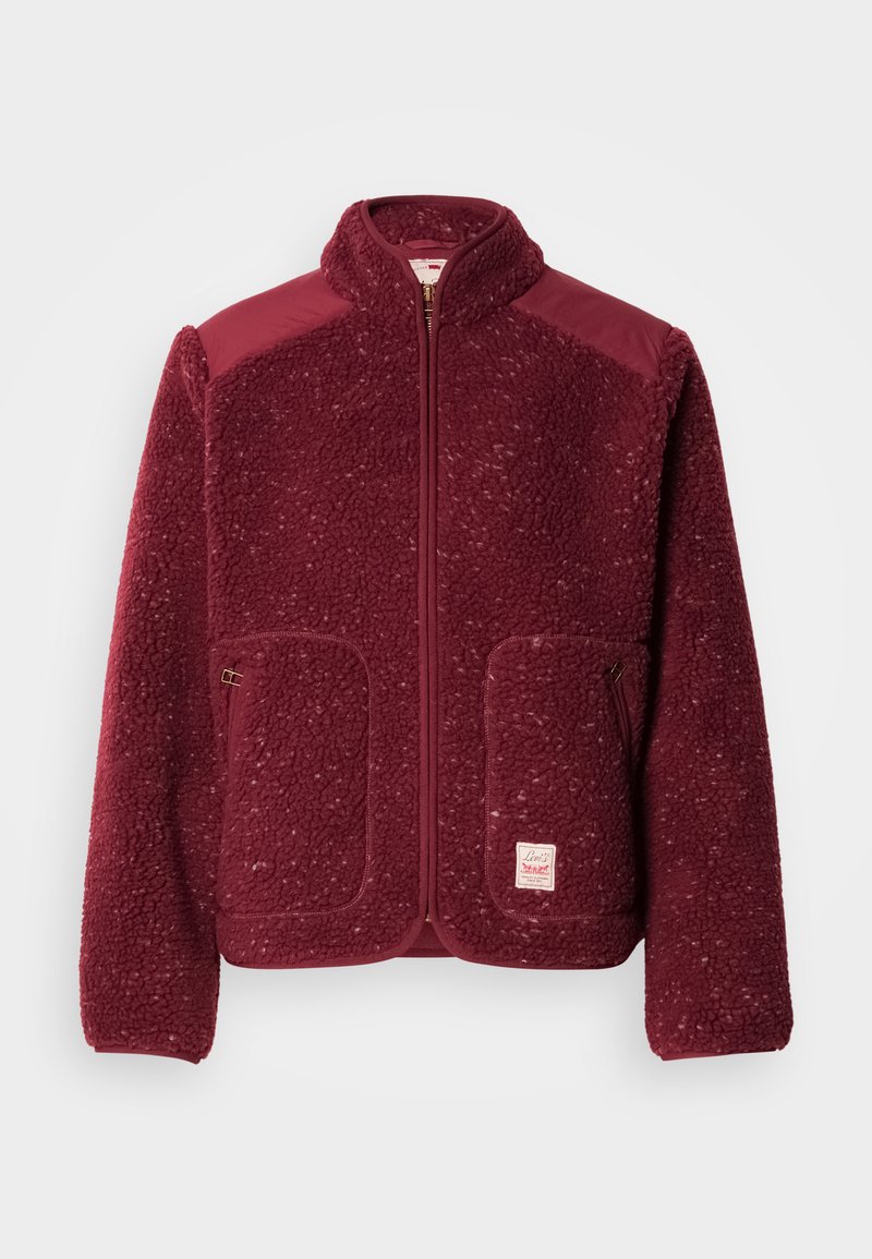 Burgundy fleece jacket with a smooth upper section, zip closure, two front pockets, and a logo patch on the lower left side.