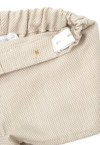 Tissu tissé beige avec un subtil motif en diamant. Présente une taille froncée avec une fermeture velcro et un petit accent doré.