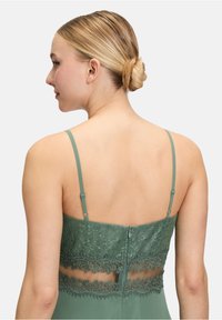 Zielona sukienka z koronki z regulowanymi cienkimi ramiączkami, z misternymi detalami koronkowymi w okolicy talii oraz z zapięciem na zamek z tyłu.