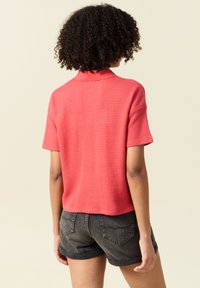 Kortärmad, korallfärgad stickad polo med ett strukturerat mönster, med krage och avkortad design, ihop med mörkblå denimshorts.