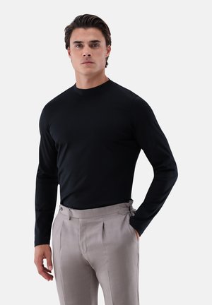 Black long-sleeve shirt with a high neckline, paired with light gray pleated trousers featuring distinctive side hardware accents.