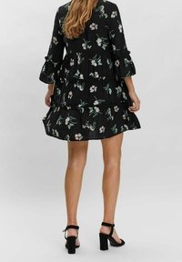 Svart blommig klänning med lager-på-lager-design, klockärm och små rosa och gröna mönster. Bärs med svarta blockklackade sandaler.