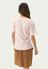 T-shirt rosa chiaro a maniche corte con spalle arricciate, abbinato a una gonna in suede marrone. Tessuto morbido con una vestibilità rilassata e scollo rotondo.