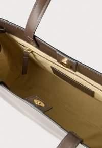 Rjava usnjena torbica s kovinskimi zlato obdelanimi detajli in bež notranjostjo. Vsebuje žep z zadrgo in dva notranja drsna žepa. Gladek tekstura.