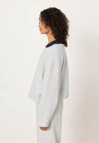 Hall hallitatud pusa musta ümar-kaelusega, pikkade varrukate ja pehme tekstuuriga, sobitatud sama halli allosaga. Lihtne disain.