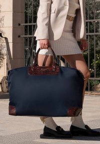 Marineblauer Stoff-Shopper mit braunen Lederakzenten und -griffen; zeichnet sich durch eine strukturierte Form und texturierte Details auf der Vorderseite aus.