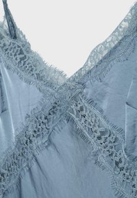 Tissu bleu clair avec bordure en dentelle florale croisée formant un décolleté en V sur un vêtement.