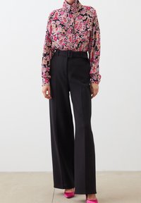 Floral blouse with pink, red, and yellow patterns; paired with high-waisted black wide-leg trousers; worn with bright pink heels.