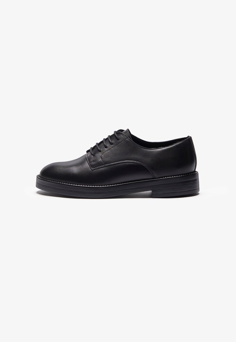 Chaussure habillée pour homme en cuir noir avec fermeture à lacets et petit talon empilé, présentée en profil sur fond blanc.