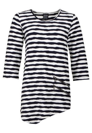 Dryžuota tunika tamsiai mėlyna ir balta, su apvalia kaklo iškirpte ir trimis ketvirčių ilgumo rankovėmis. Turizmo dvi užtrauktukų kišenės asimetriniame žalioje.