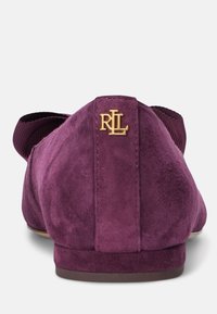 Sabrinas de camurça roxa com uma faixa elástica canelada e um logótipo monogramado dourado. Textura suave e forma arredondada, desenhadas para conforto.