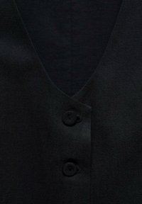 Tissu noir avec deux boutons recouverts et un col en V, montrant un gros plan de l'avant d'un vêtement.