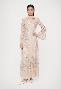 Μακρύ φλοράλ φόρεμα από διάφανο ελαφρύ μπεζ ύφασμα, με ροζ και πράσινη κεντητική διακόσμηση, μακριά φουρό μανίκια και λεπτομέρεια matching scarf.