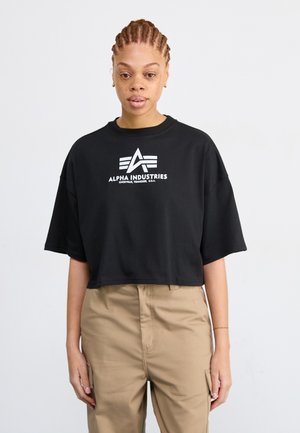 Mustat lyhythihaiset t-paidat, jotka on valmistettu puuvillasta, ja joissa on valkoinen Alpha Industries -logo geometristen yksityiskohtien kera edessä. Yhdistetty khaki-housujen kanssa.